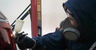 Ağır çekimde, elinde sprey tabanca ve koruyucu gözlüklü bir solunum cihazıyla çalışan bir erkek (erkek), elinde klasörlü bir el feneri ile bir araba motorunu kontrol eder. Otomatik merkez kavramı.