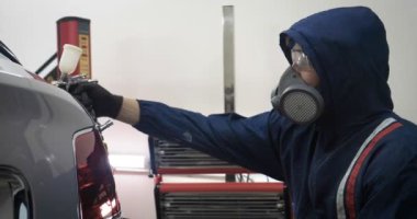 Ağır çekimde, elinde sprey tabanca ve koruyucu gözlüklü bir solunum cihazıyla çalışan bir erkek (erkek), elinde klasörlü bir el feneri ile bir araba motorunu kontrol eder. Otomatik merkez kavramı.