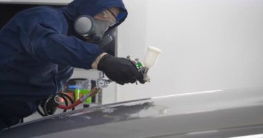 Ağır çekimde, elinde sprey tabanca ve koruyucu gözlüklü bir solunum cihazıyla çalışan bir erkek (erkek), elinde klasörlü bir el feneri ile bir araba motorunu kontrol eder. Otomatik merkez kavramı.