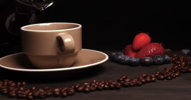 在木桌的背景 咖啡豆的心脏在它可以看到一杯 咖啡酿造 咖啡蒸汽 托盘上的下一个是羊角面包和水果 草莓和蓝莓周围 — 图库视频影像