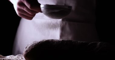 Fırında, taze ekmek pişirdikten sonra bir fırın ekmeğin üzerine toz tozu (un) toz kevgir (elleriyle) serpiştirir. Kavramı: Taze ekmek, Ev yapımı, eller, Yavaş Hareket.