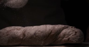 Fırında, taze ekmek pişirdikten sonra bir fırın ekmeğin üzerine toz tozu (un) toz kevgir (elleriyle) serpiştirir. Kavramı: Taze ekmek, Ev yapımı, eller, Yavaş Hareket.