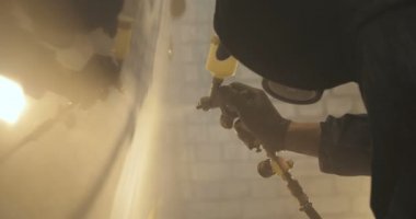 Yavaş hareket profesyonel bir adam (adam) bir garaj (hizmet) bir kazak giymiş çalışma giysileri içinde bir boya tabancası (püskürtme tabancası) ayarlar ve (seramik bir tabaka koyarak) bir yat boyama başlar.