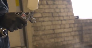 Yavaş hareket profesyonel bir adam (adam) bir garaj (hizmet) bir kazak giymiş çalışma giysileri içinde bir boya tabancası (püskürtme tabancası) ayarlar ve (seramik bir tabaka koyarak) bir yat boyama başlar.