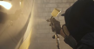 Yavaş hareket profesyonel bir adam (adam) bir garaj (hizmet) bir kazak giymiş çalışma giysileri içinde bir boya tabancası (püskürtme tabancası) ayarlar ve (seramik bir tabaka koyarak) bir yat boyama başlar.