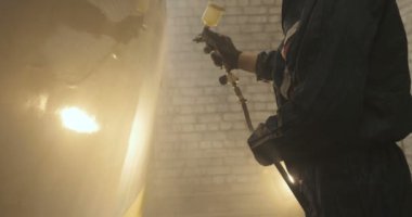 Yavaş hareket profesyonel bir adam (adam) bir garaj (hizmet) bir kazak giymiş çalışma giysileri içinde bir boya tabancası (püskürtme tabancası) ayarlar ve (seramik bir tabaka koyarak) bir yat boyama başlar.