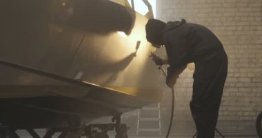 Yavaş hareket profesyonel bir adam (adam) bir garaj (hizmet) bir kazak giymiş çalışma giysileri içinde bir boya tabancası (püskürtme tabancası) ayarlar ve (seramik bir tabaka koyarak) bir yat boyama başlar.