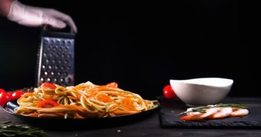 Evde pişirilen yemek (restoranda) aşçı bitmiş makarna tabağını rendelenmiş parmesan peyniri ile mutfak rendesinde süslüyor ve sos ekliyor. Peynir, muhteşem yemek, ağır çekim kavramı.