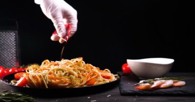 Evde pişirilen yemek (restoranda) aşçı bitmiş makarna tabağını rendelenmiş parmesan peyniri ile mutfak rendesinde süslüyor ve sos ekliyor. Peynir, muhteşem yemek, ağır çekim kavramı.