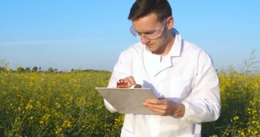 Genç yakışıklı (erkek) biyolog veya agronomist, beyaz bir ceket, gözlük, mavi lastik eldiven, elma ağacı boyunca yürür nem yaprakları, DNA, pipet, analizleri alır. Yakışıklı biyolog veya beyaz tıbbi giysiler, güvenlik gözlükleri içinde agronomist.