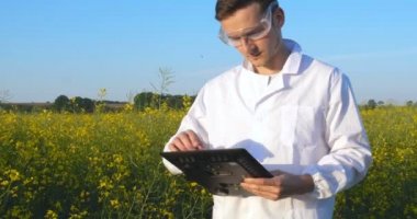 Genç yakışıklı (erkek) biyolog veya agronomist, beyaz bir ceket, gözlük, mavi lastik eldiven, elma ağacı boyunca yürür nem yaprakları, DNA, pipet, analizleri alır. Yakışıklı biyolog veya beyaz tıbbi giysiler, güvenlik gözlükleri içinde agronomist.