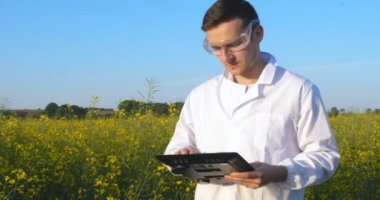 Genç yakışıklı (erkek) biyolog veya agronomist, beyaz bir ceket, gözlük, mavi lastik eldiven, elma ağacı boyunca yürür nem yaprakları, DNA, pipet, analizleri alır. Yakışıklı biyolog veya beyaz tıbbi giysiler, güvenlik gözlükleri içinde agronomist.