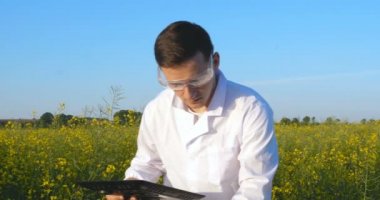 Genç yakışıklı (erkek) biyolog veya agronomist, beyaz bir ceket, gözlük, mavi lastik eldiven, elma ağacı boyunca yürür nem yaprakları, DNA, pipet, analizleri alır. Yakışıklı biyolog veya beyaz tıbbi giysiler, güvenlik gözlükleri içinde agronomist.