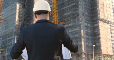 Genç bir adam (erkek) mimar, takım elbiseli bir işadamı, elinde tabletli bir klasör (cep telefonu) olan bir ceket içinde inşaat alanını ve iş binasını çeşitli eylemlerle kontrol ediyor..