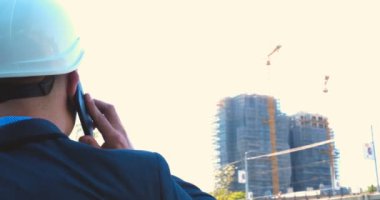 Genç bir adam (erkek) mimar, takım elbiseli bir işadamı, elinde tabletli bir klasör (cep telefonu) olan bir ceket içinde inşaat alanını ve iş binasını çeşitli eylemlerle kontrol ediyor..