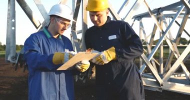 Bir elektrikçi veya Oluşturucusu ve mühendis, sarı ve beyaz kask içinde mavi bir elbise içinde güç için teknik genel bakış kontrol, elektrik direkleri, bir elektrik Kulesi, enerji ve işçi hazırlamak.