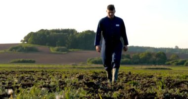 Yeşil ve sarı bokeh arka plan ile verimli topraklarda büyüyen çiftçi ve besleyici ağaç elleri. Genç bir adam (adam), çalışan üniformalı bir çiftçi, lastik çizmeler bir alanda yürüyor. Kavramı: Özgürlük, Kauçuk çizmeler, Yaşam Tarzı, Çiftçi.