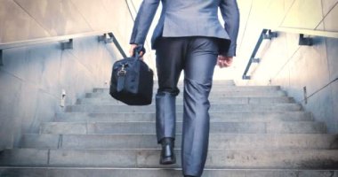 Genç yakışıklı adam (adam) işadamı ayakta (oturan) bir takım elbiseli bir ağacın yanında. Elinde siyah bir çantayla merdivenleri tırmanıyor. Konsept: iş, takım elbise, adam, adam, çanta, işadamı.