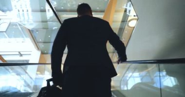 Genç yakışıklı adam (adam) işadamı ayakta (oturan) bir takım elbiseli bir ağacın yanında. Elinde siyah bir çantayla merdivenleri tırmanıyor. Konsept: iş, takım elbise, adam, adam, çanta, işadamı.