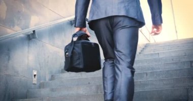 Genç yakışıklı adam (adam) işadamı ayakta (oturan) bir takım elbiseli bir ağacın yanında. Elinde siyah bir çantayla merdivenleri tırmanıyor. Konsept: iş, takım elbise, adam, adam, çanta, işadamı.