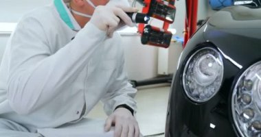 Profesyonel bir erkek (çocuk) arabanın seramik ustası çekmeceye fiber (sünger) bez kullanarak arabanın üzerine seramik koyar, güvenlik gözlükleri ve siyah eldivenler takar ve boya (çizikler) ve boya kompozisyonu (çizikler) için boya yaptıktan sonra arabayı tamamen kontrol eder.