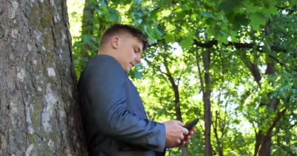 年轻的帅哥 商人站在 在树旁西装 手里拿着一个黑色的包爬楼梯 — 图库视频影像