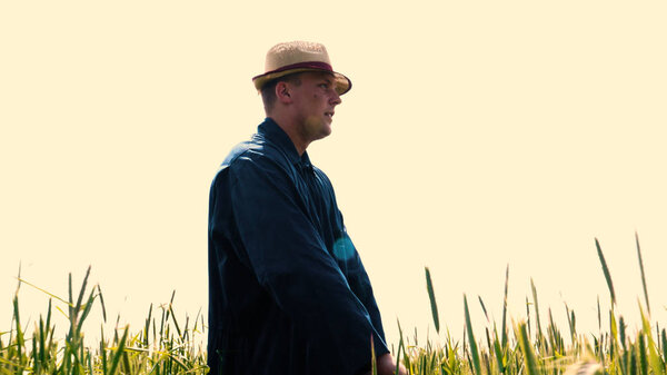 Portrait of a young guy (man) in a working uniform and a straw hat in the middle of a field around wheat and hay, running around it and checking the wheat for maturity, heat field in a shirt and straw hat breathes in the fresh air and feels free. Con