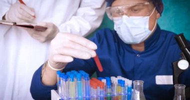 Simyacı, şişeler tutan, bir testin farklı kompozisyonlar, beyaz önlük, solunum, Gözlük, beyaz eldivenleri, yeşil bir arka plan ile test tüpleri testleri.