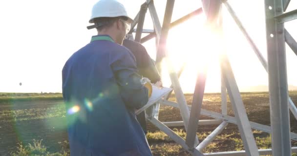 一个电工或建设者和工程师 在蓝色长袍 在一个黄色和白色的头盔 检查强度的技术概述 准备电线杆 能源和工人 — 图库视频影像