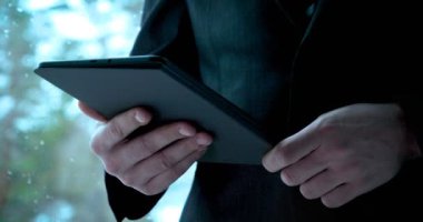 Takım elbiseli genç bir adam (Man) işadamı, caddenin arka planında bir telefon tutarak toplantı bekliyor. Takım elbiseli işadamı binada telefon (tablet) tutarak konuşuyor.