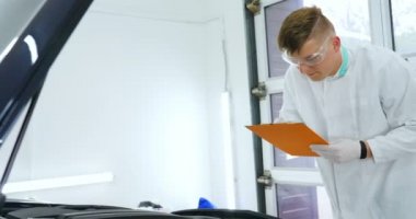 Profesyonel bir erkek (çocuk) arabanın seramik ustası çekmeceye fiber (sünger) bez kullanarak arabanın üzerine seramik koyar, güvenlik gözlükleri ve siyah eldivenler takar ve boya (çizikler) ve boya kompozisyonu (çizikler) için boya yaptıktan sonra arabayı tamamen kontrol eder.