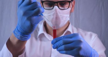 Laboratuar çalışması, Doktor bir pipet tutan, bir tıbbi maske ve gözlük, mavi kauçuk eldiven bir test tüpü bir test alır, analiz, kan, DNA, bir test tüp tutucu.