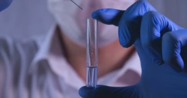 Laboratuar çalışması, Doktor bir pipet tutan, bir tıbbi maske ve gözlük, mavi kauçuk eldiven bir test tüpü bir test alır, analiz, kan, DNA, bir test tüp tutucu.