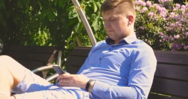 Adam parkta bir ağacın altında, suyun yanında bir tablet bilgisayar kullanıyor. Arka planda şehir manzarası. Seçici odak, tonda görüntü, yakışıklı genç beyaz turist adam mutlu ve bir selfie alarak heyecanlı, çekici genç Kafkas turist öğrenci adam hav