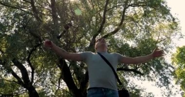 Adam parkta bir ağacın altında, suyun yanında bir tablet bilgisayar kullanıyor. Arka planda şehir manzarası. Seçici odak, tonda görüntü, yakışıklı genç beyaz turist adam mutlu ve bir selfie alarak heyecanlı, çekici genç Kafkas turist öğrenci adam hav