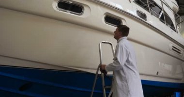 Genç yakışıklı profesyonel adam (erkek) temizleyici, yat parlatma ve astar seramikten sonra yat yıkıyor. Yat teknisyeni, çamurdan bir kimyasal sprey (boya) temizleyici kullanarak pervaneyi temizler. Konsept: yeni teknik, kimya, Profesi