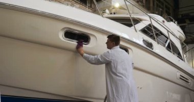 Genç yakışıklı profesyonel adam (erkek) temizleyici, yat parlatma ve astar seramikten sonra yat yıkıyor. Yat teknisyeni, çamurdan bir kimyasal sprey (boya) temizleyici kullanarak pervaneyi temizler. Konsept: yeni teknik, kimya, Profesi
