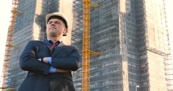 一个成功的年轻英俊工程师 建筑师 建筑商 戴着白色头盔 身穿西服 手持记事本 背景和建筑的画像 — 图库视频影像