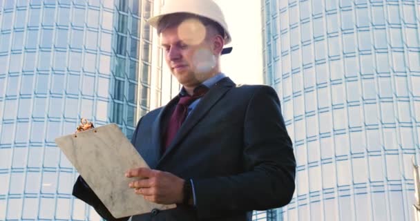 一位年轻的建筑师 穿着工作服 身穿夹克衫 手里拿着平板电脑 用各种行动检查建筑工地和商业大楼 — 图库视频影像