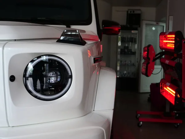 Infrared drying of car body parts after applying putty and paint on a white off-road vehicle in the body repair shop with red lanterns in the working environment. Concept of: Car Ceramic, Slow Motion.