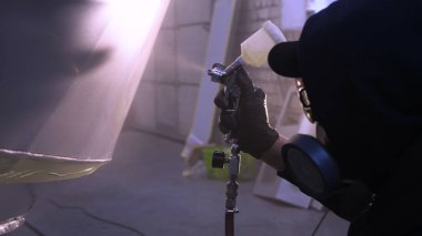 Garajda profesyonel bir adam (adam) bir mini-jet (spreyler) ile bir koruyucu takım dispenser ve koruyucu gözlük kullanarak yüzeye boya (seramik) uygulayarak yat (ulaşım) kapsar.