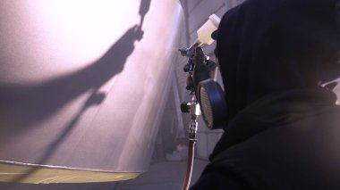 Garajda profesyonel bir adam (adam) bir mini-jet (spreyler) ile bir koruyucu takım dispenser ve koruyucu gözlük kullanarak yüzeye boya (seramik) uygulayarak yat (ulaşım) kapsar.