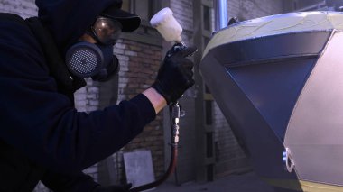 Garajda profesyonel bir adam (adam) bir mini-jet (spreyler) ile bir koruyucu takım dispenser ve koruyucu gözlük kullanarak yüzeye boya (seramik) uygulayarak yat (ulaşım) kapsar.