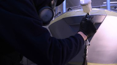 Garajda profesyonel bir adam (adam) bir mini-jet (spreyler) ile bir koruyucu takım dispenser ve koruyucu gözlük kullanarak yüzeye boya (seramik) uygulayarak yat (ulaşım) kapsar.