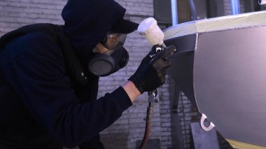 Garajda profesyonel bir adam (adam) bir mini-jet (spreyler) ile bir koruyucu takım dispenser ve koruyucu gözlük kullanarak yüzeye boya (seramik) uygulayarak yat (ulaşım) kapsar.