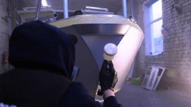 Garajda profesyonel bir adam (adam) bir mini-jet (spreyler) ile bir koruyucu takım dispenser ve koruyucu gözlük kullanarak yüzeye boya (seramik) uygulayarak yat (ulaşım) kapsar.