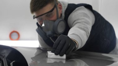 Profesyonel bir erkek (erkek) bir araba seramik ustası bir çekmece, güvenlik gözlükleri ve siyah eldiven bir fiber (sünger) bez kullanarak bir araba seramik koyar.