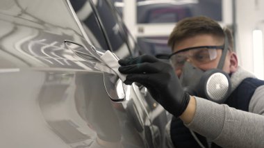 A professional male (boy) master of ceramics of a car puts ceramics on a car using a fiber (sponge) rag in a puller, safety goggles and black gloves. clipart