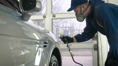 Elinde sprey tabancaları ile çalışan üniforma lı profesyonel ve koruyucu gözlüklü bir solunum cihazı arabanın farklı yerlerine boya (seramik) koyar, elinde bir klasör ile el feneri servis edilebilirlik için bir araba motoru kontrol eder. Kavram 