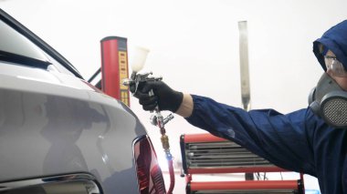 Elinde sprey tabancaları ile çalışan üniforma lı profesyonel ve koruyucu gözlüklü bir solunum cihazı arabanın farklı yerlerine boya (seramik) koyar, elinde bir klasör ile el feneri servis edilebilirlik için bir araba motoru kontrol eder. Kavram 